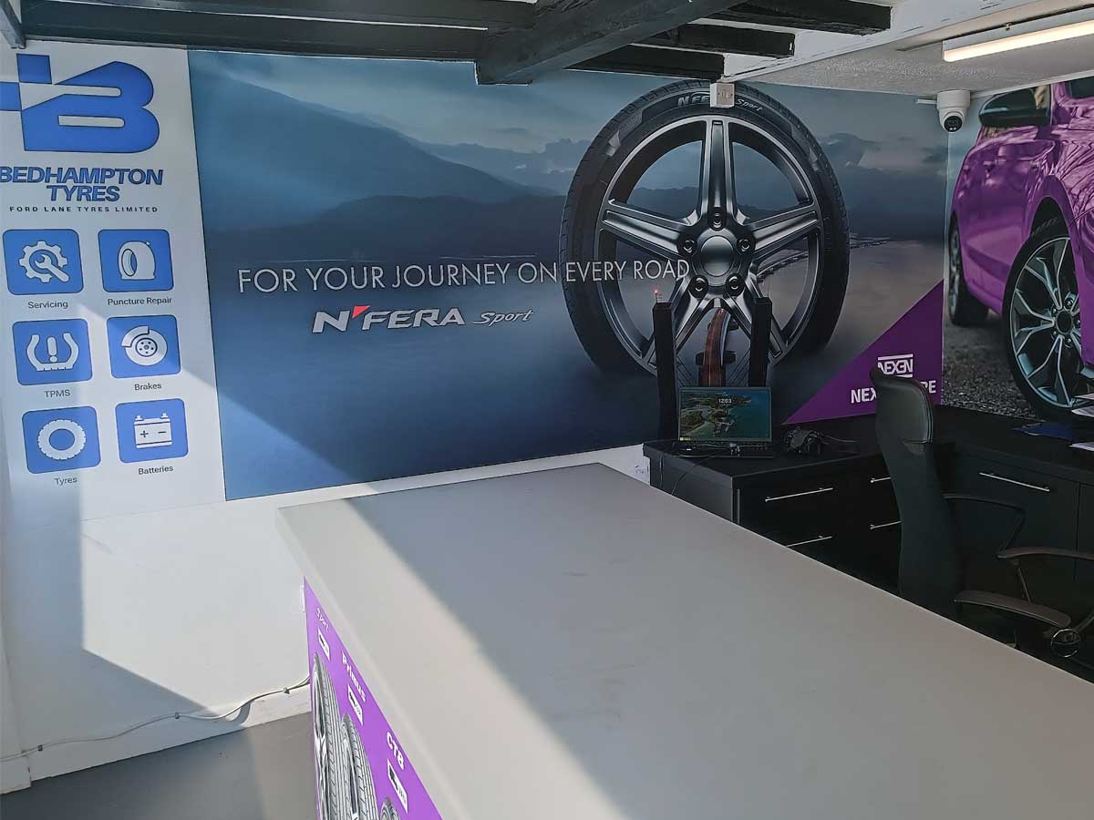 Internal view of the reception area for at Bedhampton Tyres showing a decorative large wall covering for Nexen Tyres and a poster showing the services available